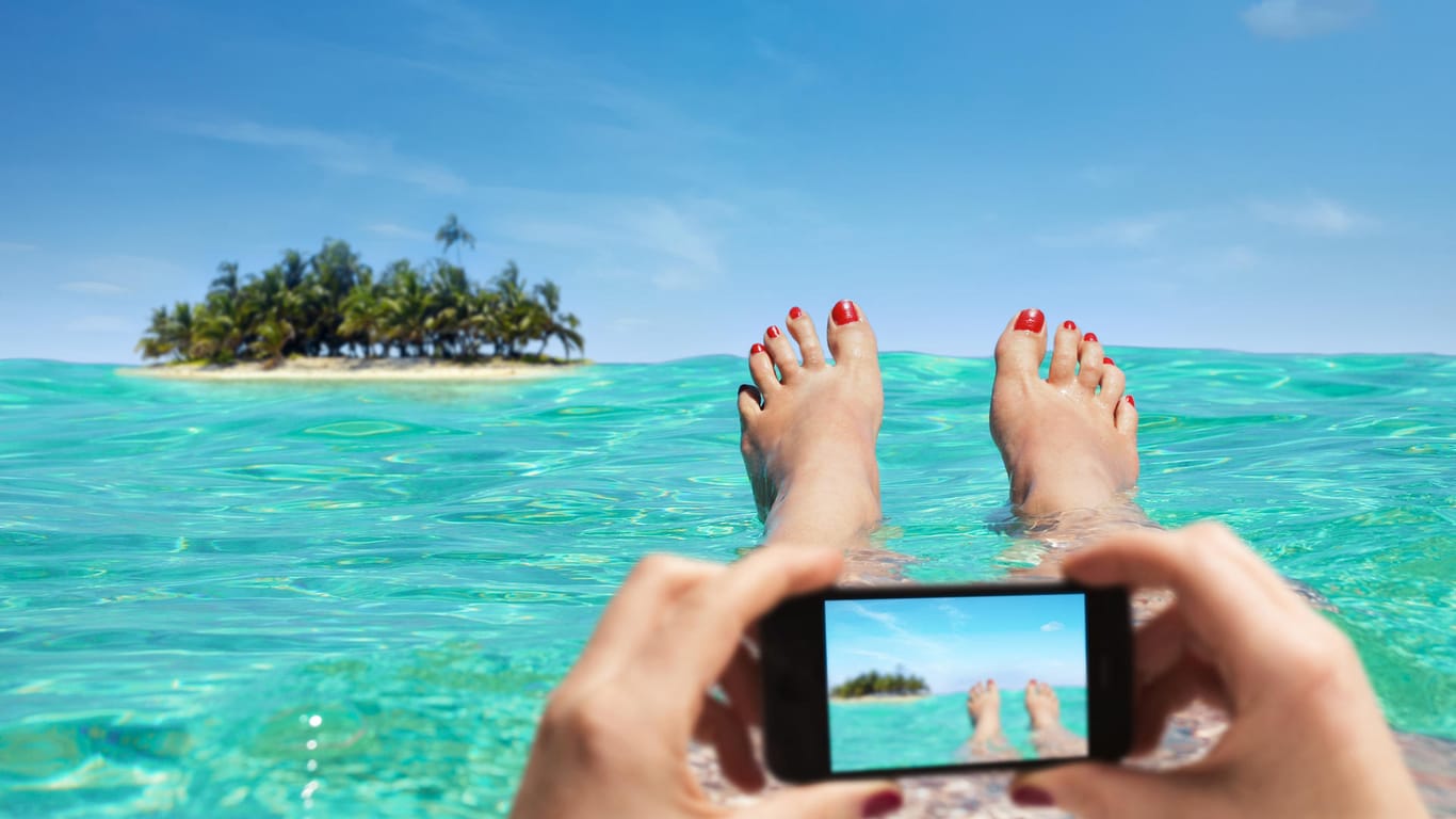 Eine Frau macht ein Foto am Strand: Wer Urlaubsbilder postet, macht damit öffentlich, dass seine Wohnung derzeit unbewacht ist.