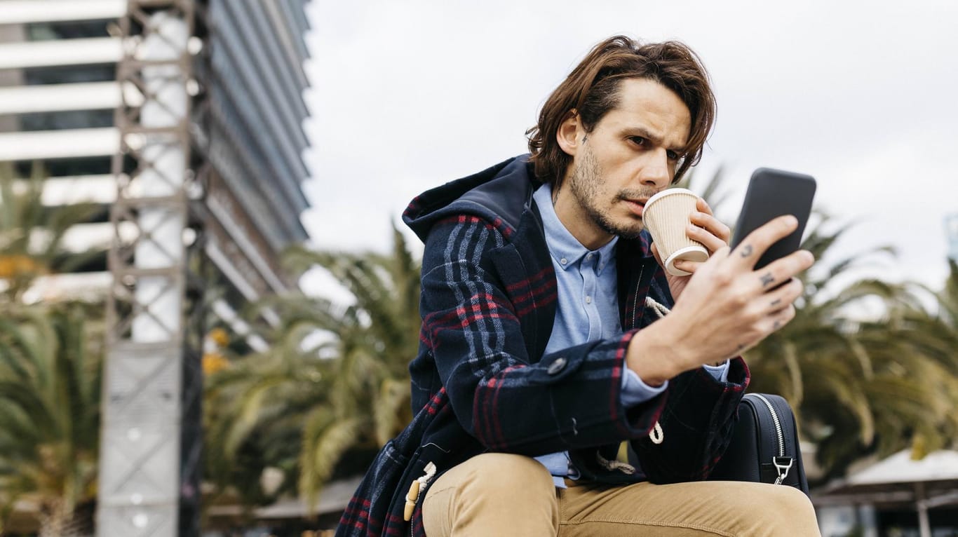 Ein Mann trinkt Kaffee und schaut auf sein Smartphone: Viele Billig-Tarife klingen nur auf den ersten Blick attraktiv.