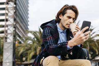 Ein Mann trinkt Kaffee und schaut auf sein Smartphone: Viele Billig-Tarife klingen nur auf den ersten Blick attraktiv.