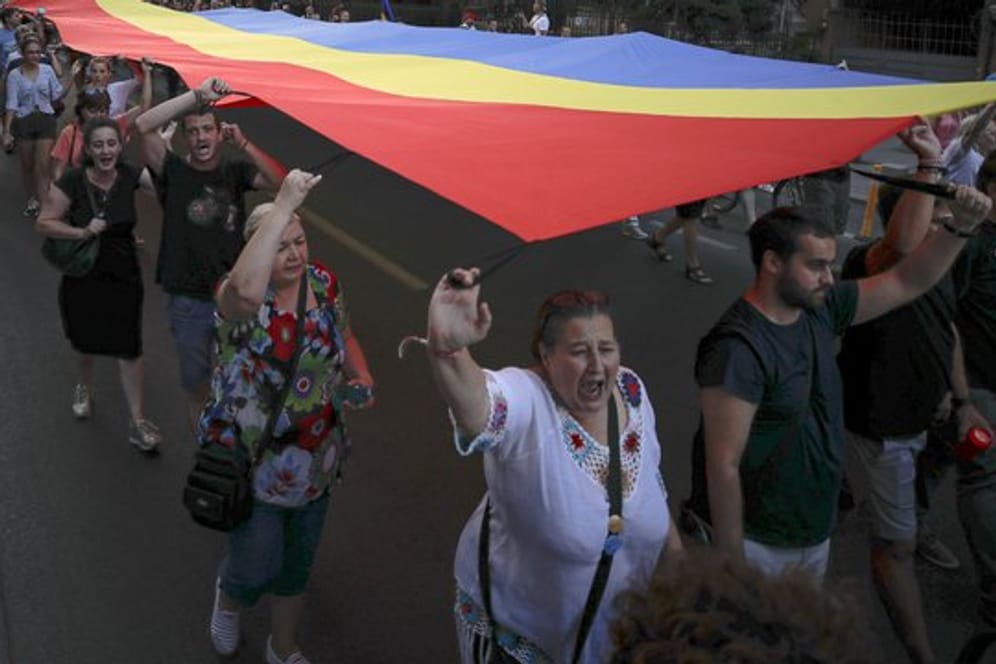 Menschen halten eine rumänische Flagge während einer Demonstration zum Gedenken an ein getötetes 15-jähriges Mädchen in Bukarest.