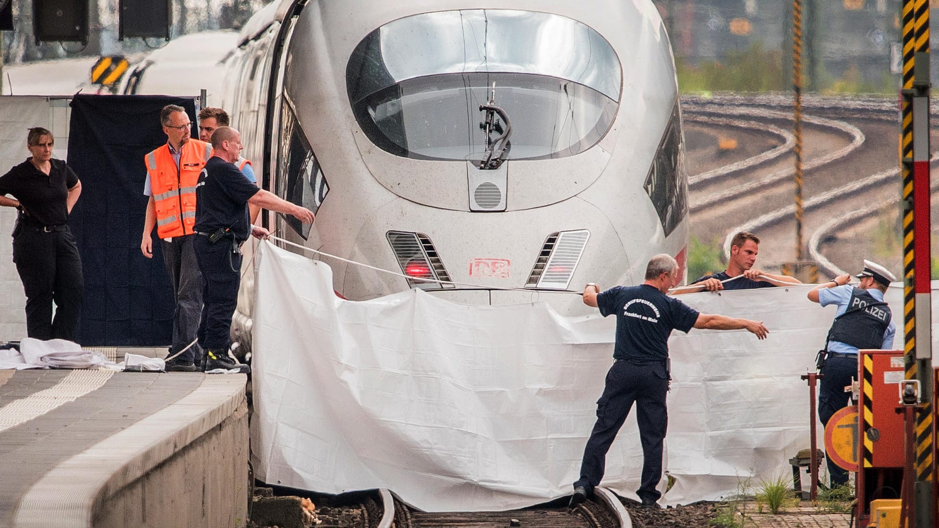 Frankfurt/Main: Polizisten und Feuerwehrleute spannen im Hauptbahnhof eine weiße Plane als Sichtschutz vor einen ICE.