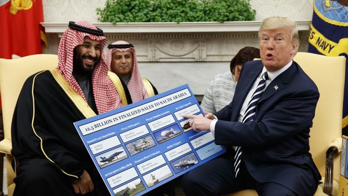 US-Präsident Donald Trump (r) empfängt den saudischen Kronprinzen Mohammed bin Salman 2018 im Weißen Haus und zeigt dabei auf ein Plakat, auf dem die Waffenverkäufe von den USA an Saudi-Arabien detailliert erklärt sind.