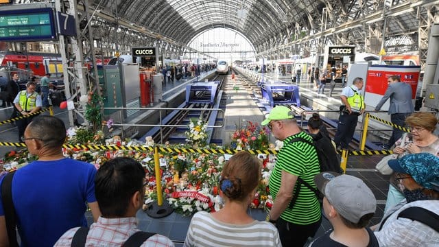 Passanten stehen am Gleis 7 des Frankfurter Hauptbahnhofs vor einem Meer aus Blumen und Kuscheltieren.