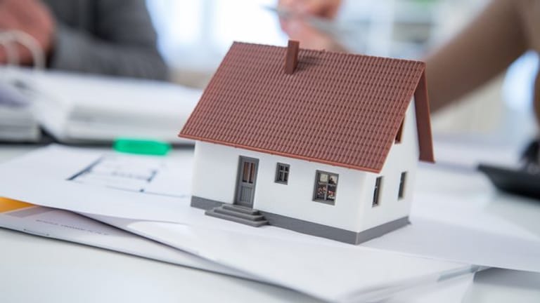 Miniaturhaus auf Unterlagen: Wer ein Haus kaufen möchte, holt vorher möglichst viele Informationen ein und prüft verfügbare Pläne.