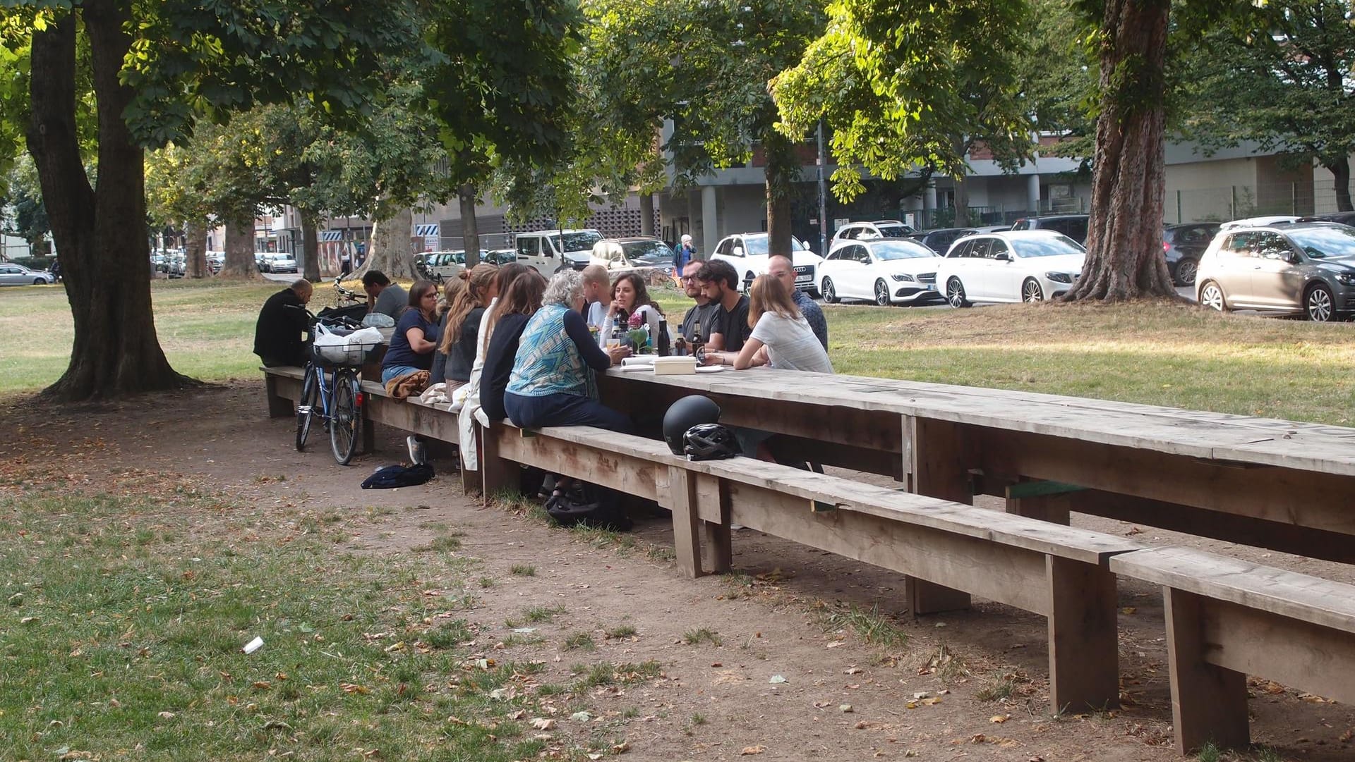 Kölner sitzen am "Langen Tisch": Der Holztisch ist rund 30 Meter lang und ein beliebter Treffpunkt. Sein Erhalt ist allerdings nicht sicher.