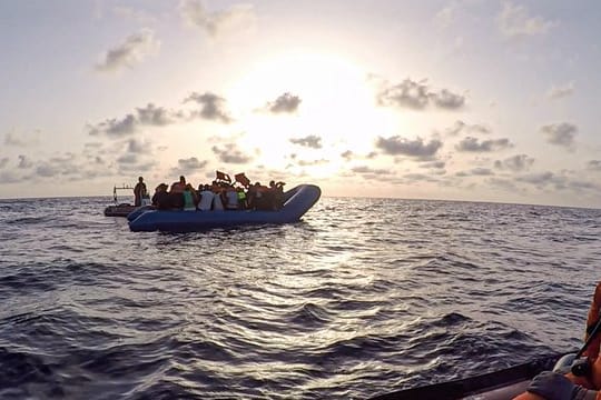 Das von der Seenotrettungsorganisation Sea-Eye herausgegebene Foto vom Mittwoch zeigt Seenotretter der "Alan Kurdi" vor einem Schlauchboot voller Flüchtlinge.