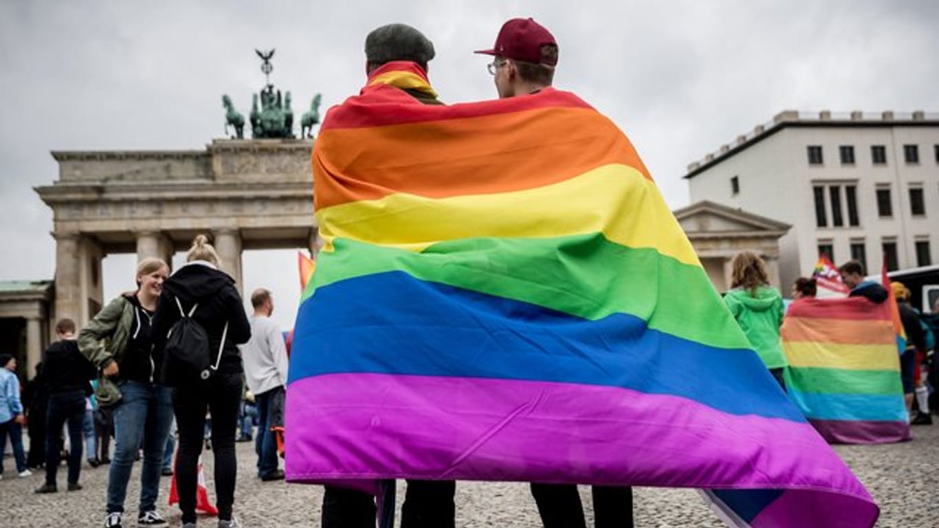 Eingehüllt in eine Regenbogenflagge, steht ein homosexuelles Paar vor dem Brandenburger Tor in Berlin.
