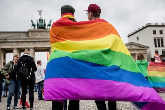 Eingehüllt in eine Regenbogenflagge, steht ein homosexuelles Paar vor dem Brandenburger Tor in Berlin.