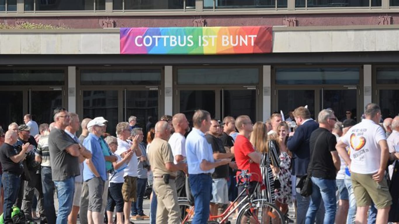 Teilnehmer des Wahlkampfauftakts der AfD-Jugendorganisation Junge Alternative stehen vor einem Transparent an der Stadthalle mit der Aufschrift "Cottbus ist bunt".