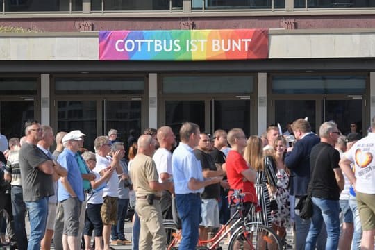 Teilnehmer des Wahlkampfauftakts der AfD-Jugendorganisation Junge Alternative stehen vor einem Transparent an der Stadthalle mit der Aufschrift "Cottbus ist bunt".