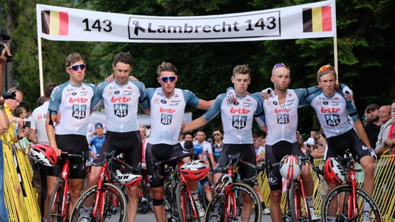 Die Fahrer des Teams Lotto Soudal stehen für eine Schweigeminute zum Tod von Bjorg Lambrecht mit Trauerflor vor einem Banner.