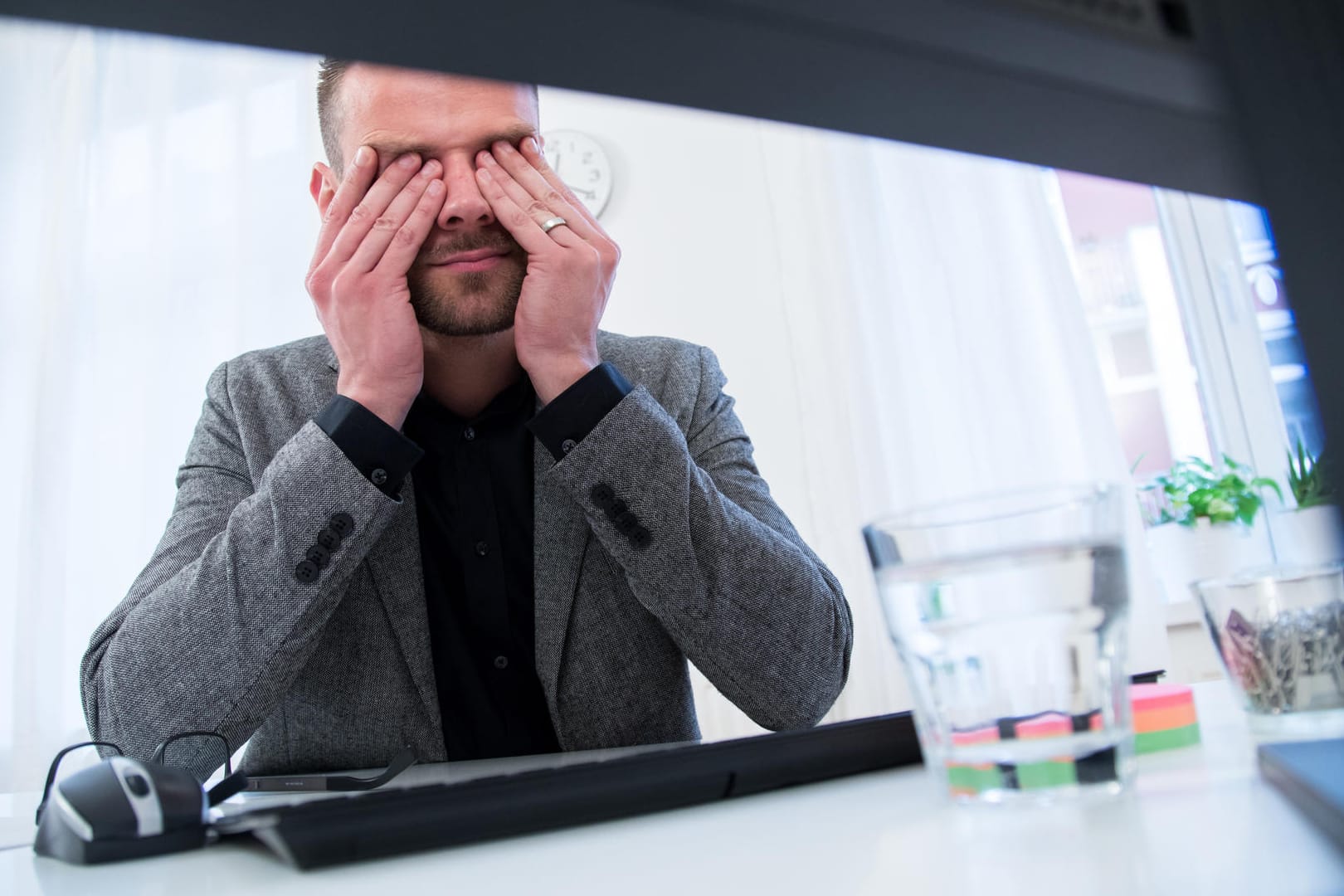 Ein Mann reibt sich die Augen: Gegen müde Augen bei der Arbeit hilft es, den richtigen Abstand zum Bildschirm einzuhalten und regelmäßig Pausen zu machen.