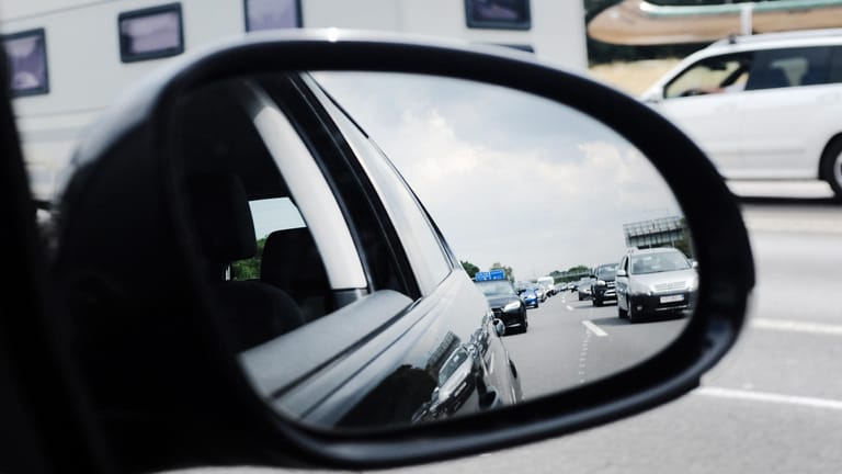Im Außenspiegel eines Autos ist ein Stau auf einer Autobahn zu sehen: Die Autoclubs rechnen am kommenden Wochenende mit vollen Straßen.