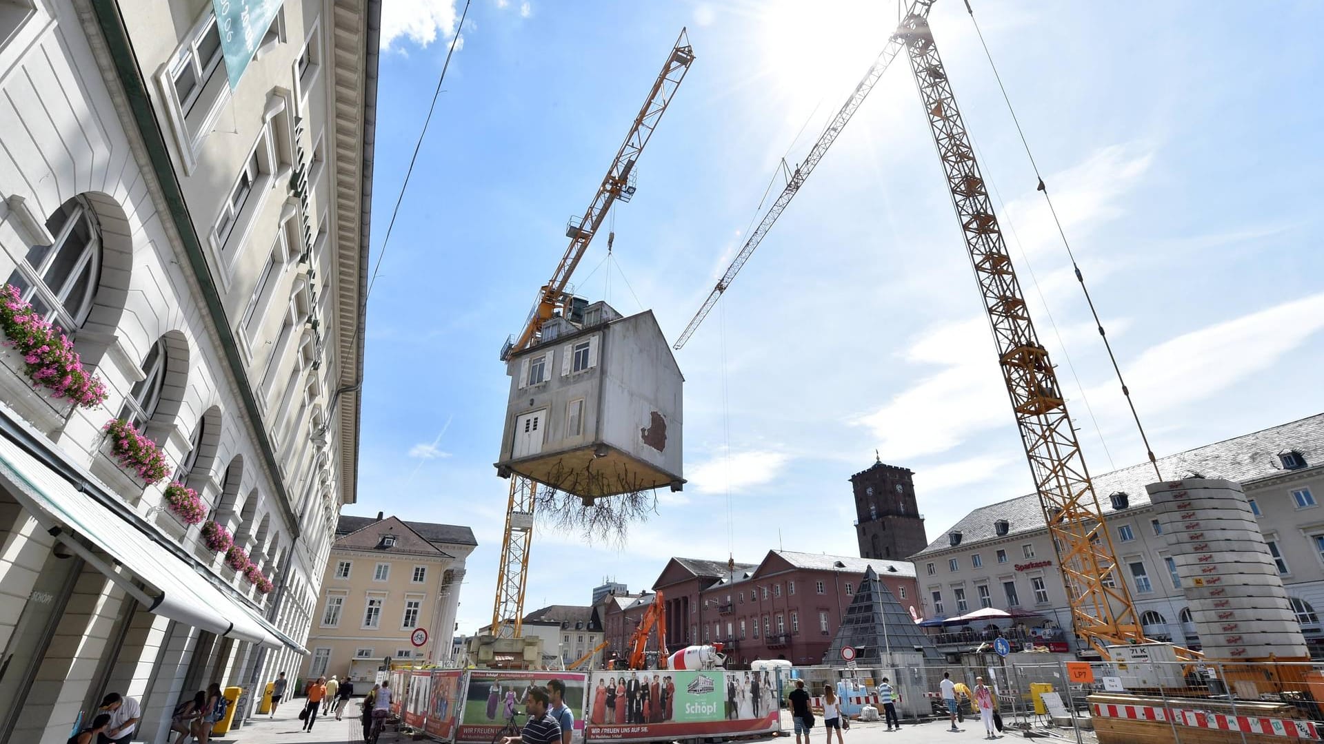 Die Karlsruher Innenstadt: Über dem Marktplatz hängt ein Haus an einem Kran.