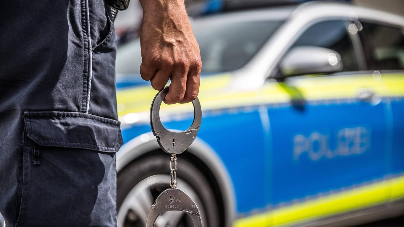 Ein Polizist mit Handschellen vor einem Streifenwagen: In Hagen soll ein Jugendlicher sich bei seiner Ingewahrsamnahme so heftig gewehrt haben, dass zwei Polizisten verletzt worden sind.