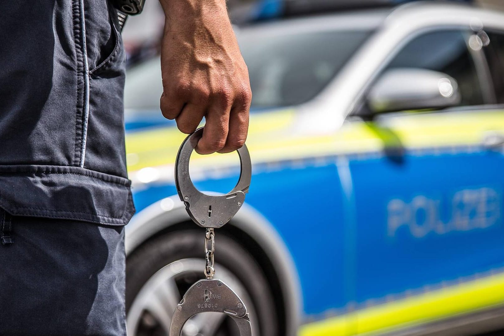 Ein Polizist mit Handschellen vor einem Streifenwagen: In Hagen soll ein Jugendlicher sich bei seiner Ingewahrsamnahme so heftig gewehrt haben, dass zwei Polizisten verletzt worden sind.