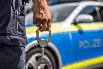 Ein Polizist mit Handschellen vor einem Streifenwagen: In Hagen soll ein Jugendlicher sich bei seiner Ingewahrsamnahme so heftig gewehrt haben, dass zwei Polizisten verletzt worden sind.