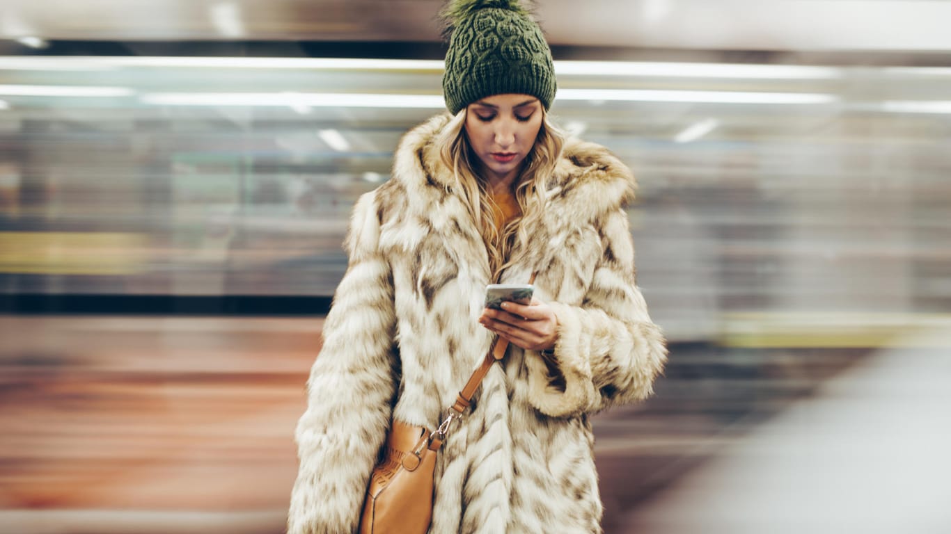 Eine junge Frau an einem Bahnhof schaut auf ihr Smartphone: Alte Mobilfunkverträge mit UMTS müssen umgestellt werden.