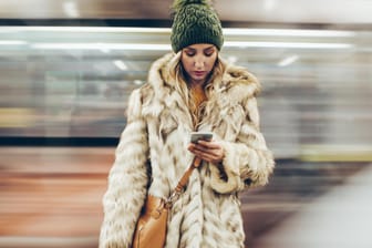 Eine junge Frau an einem Bahnhof schaut auf ihr Smartphone: Alte Mobilfunkverträge mit UMTS müssen umgestellt werden.