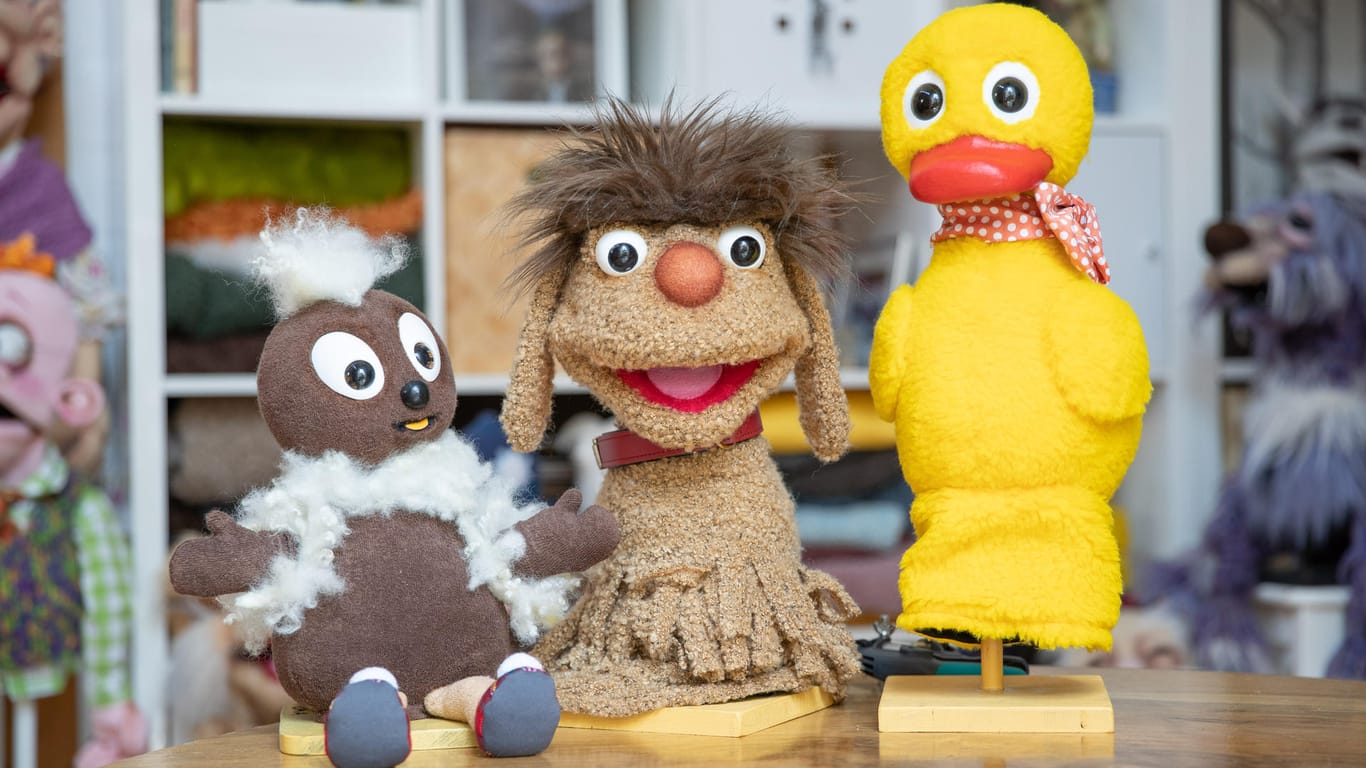Die Sandmännchen-Puppenfiguren "Pittiplatsch", "Moppi" und "Schnatterinchen" stehen nebeneinander auf einem Tisch.