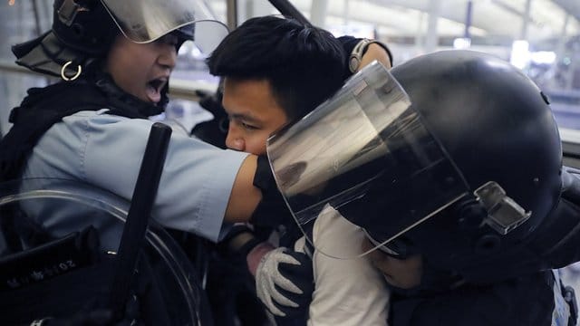 Polizisten in Schutzausrüstung nehmen einen Demonstranten im Hongkonger Flughafen fest. Polizisten in Schutzausrüstung nehmen einen Demonstranten im Hongkonger Flughafen fest.