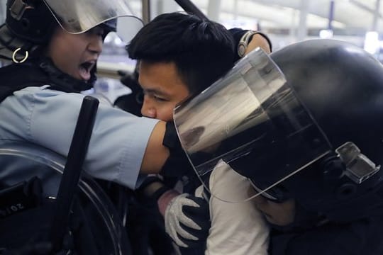 Polizisten in Schutzausrüstung nehmen einen Demonstranten im Hongkonger Flughafen fest.