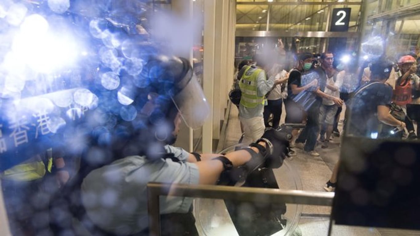 Ein Polizist richtet im Flughafen von Hongkong seine Waffe auf Demonstranten.