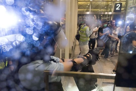 Ein Polizist richtet im Flughafen von Hongkong seine Waffe auf Demonstranten.