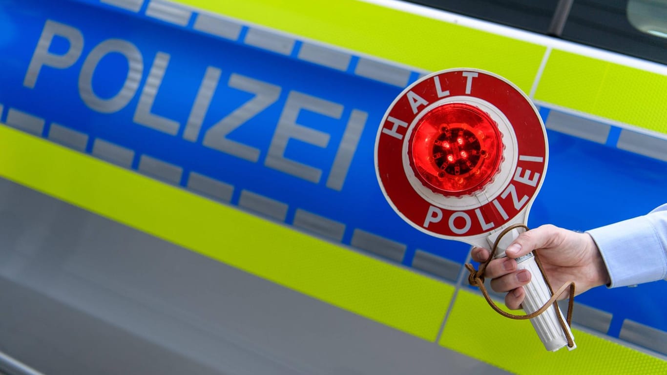 Eine Polizeikelle mit Halt Polizei vor einem Streifenwagen: In Essen hat ein Rollerfahrer auf der Flucht vor der Polizei einen Streifenwagen gerammt.