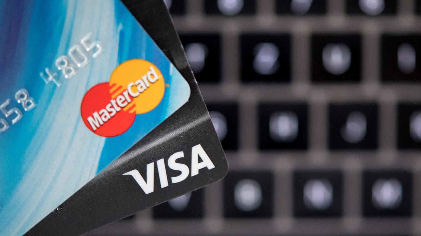 Zwei Kreditkarten werden vor dem Hintergrund einer Laptop-Tastatur in die Luft gehalten: Das Bezahlen beim Einkaufen im Internet soll sicherer werden. Nicht nur Verbraucher, auch Kreditinstitute und Online-Händler müssen sich rechtzeitig darauf einstellen.