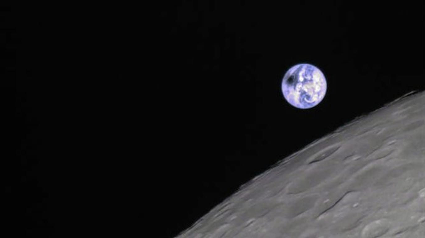 Die von Kratern zerklüftete Rückseite des Mondes vor der blauen Erde.