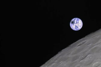Die von Kratern zerklüftete Rückseite des Mondes vor der blauen Erde.