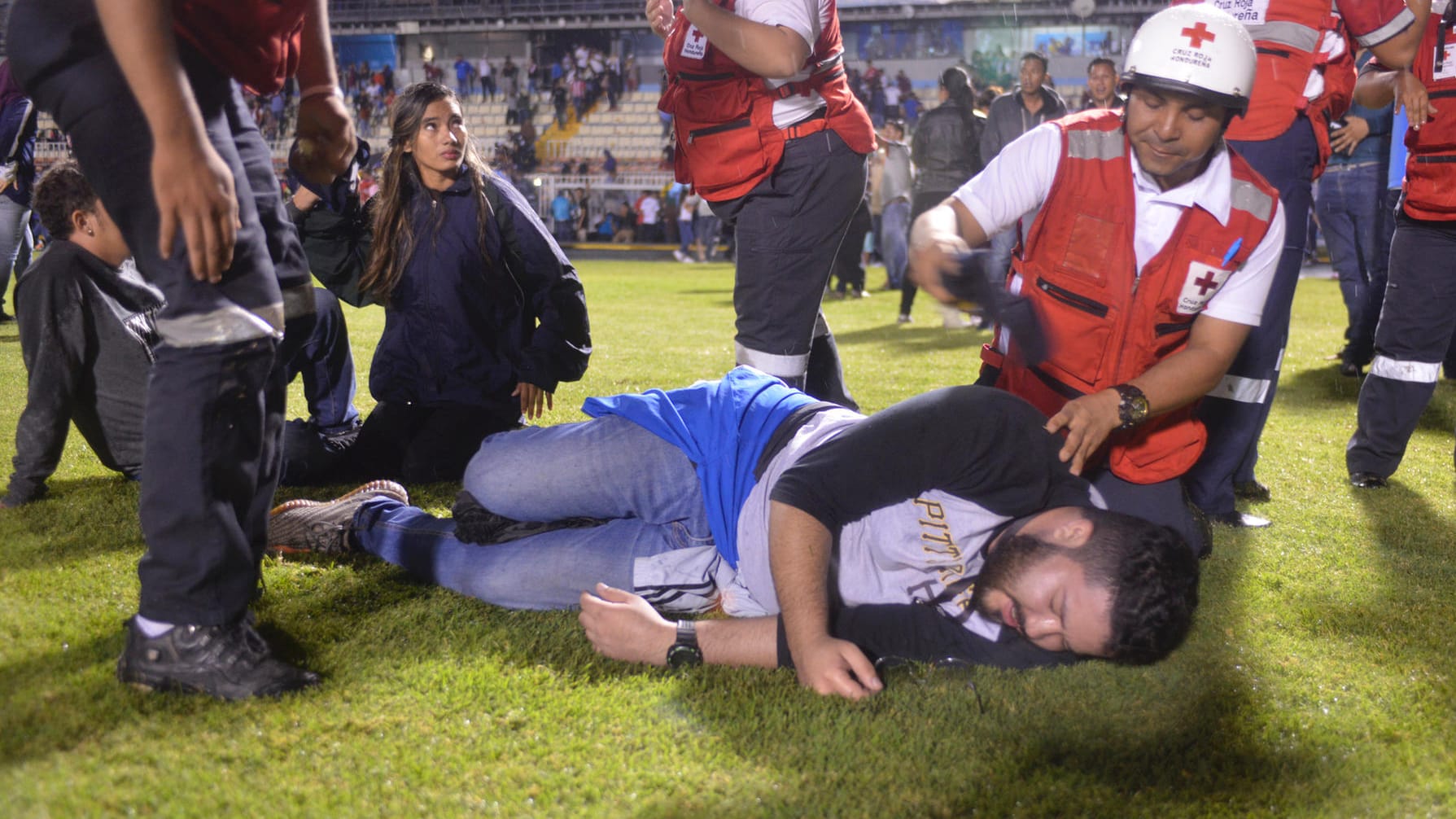 Helfer des Roten Kreuz kümmern sich um Fußballfans, die vor dem Start des Spiels zwischen Motagua and Olimpia von Tränengas verletzt wurden. Helfer des Roten Kreuz kümmern sich um Fußballfans, die vor dem Start des Spiels zwischen Motagua and Olimpia von Tränengas verletzt wurden.