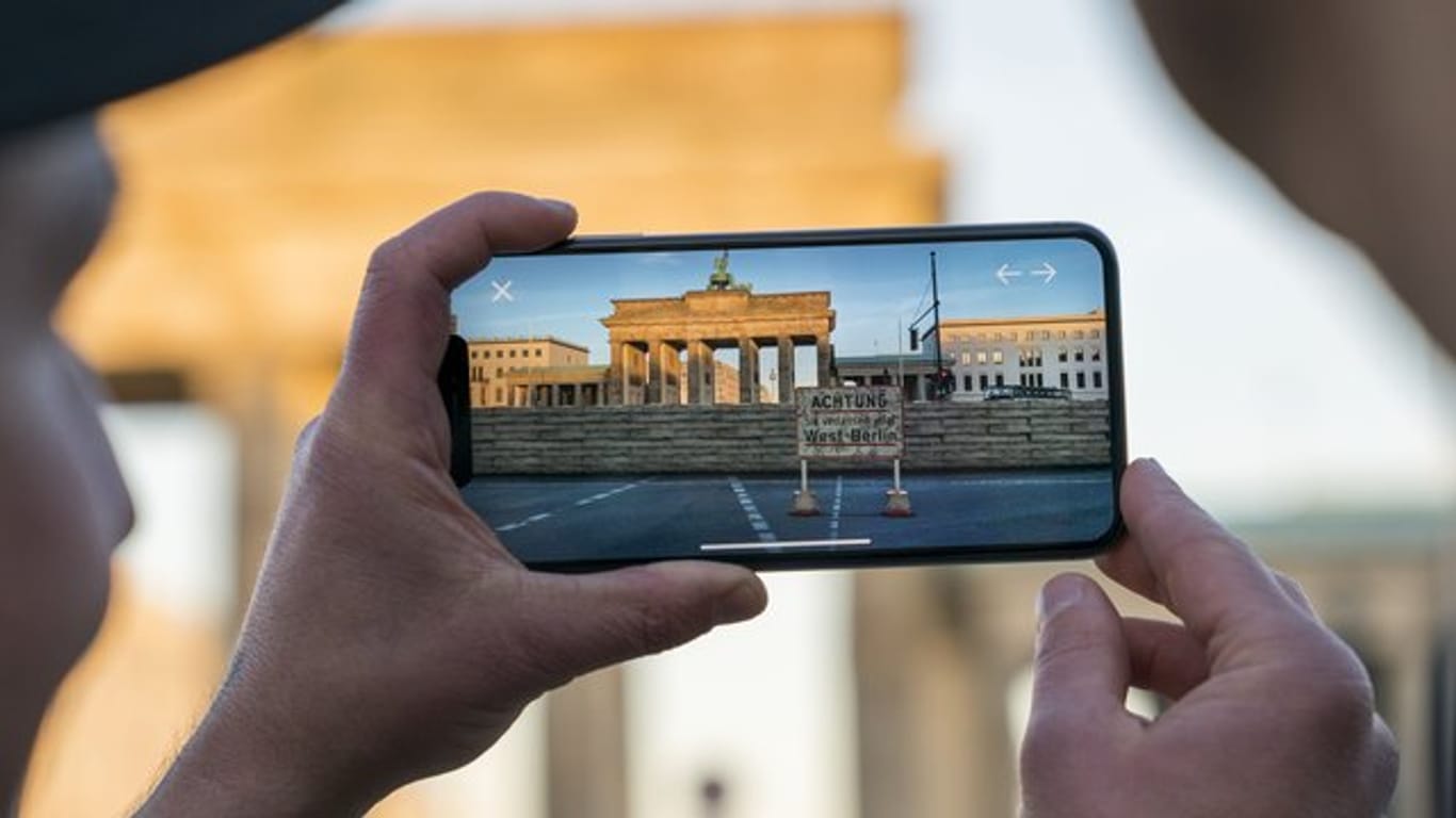 Apple-Chef Tim Cook lässt sich am Brandenburger Tor von Entwickler Peter Kolski das Projekt "MauAR" auf einem Smartphone erklären.