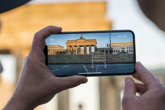 Apple-Chef Tim Cook lässt sich am Brandenburger Tor von Entwickler Peter Kolski das Projekt "MauAR" auf einem Smartphone erklären.