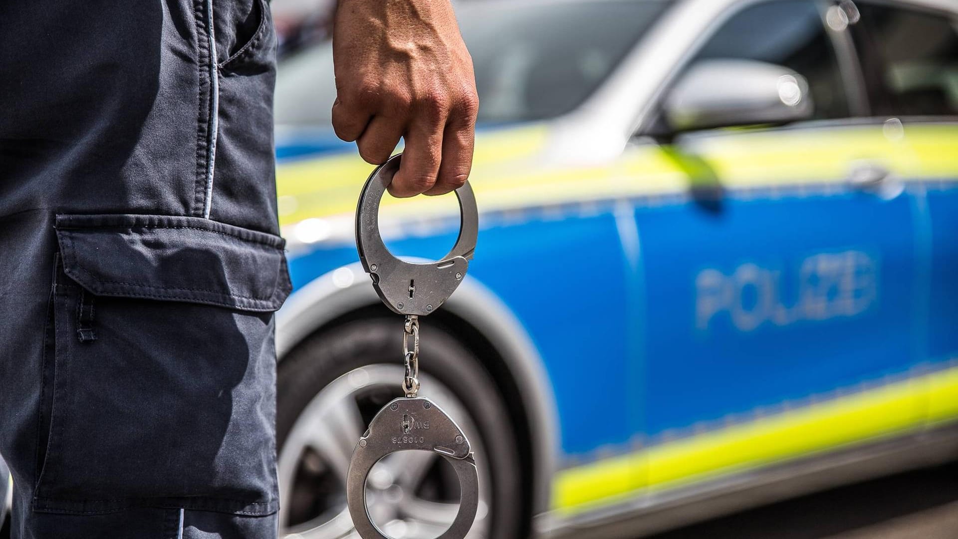 Handschellen vor einem Polizeiwagen: In Essen wurde ein 79-Jähriger festgenommen, nachdem seine Ehefrau schwer verletzt aufgefunden wurde.