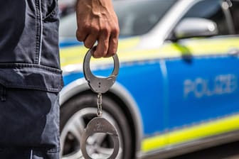 Handschellen vor einem Polizeiwagen: In Essen wurde ein 79-Jähriger festgenommen, nachdem seine Ehefrau schwer verletzt aufgefunden wurde.
