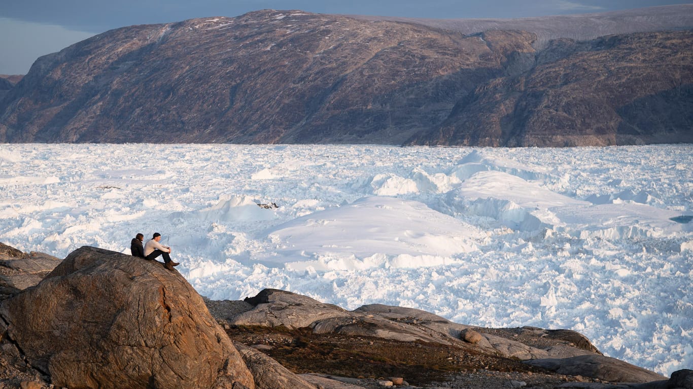 Forscher sitzen auf einem Hügel und blicken auf den Helheim-Gletscher: Von dem riesigen Gletscher in Grönland verschwinden jeden Tag ein paar Meter.