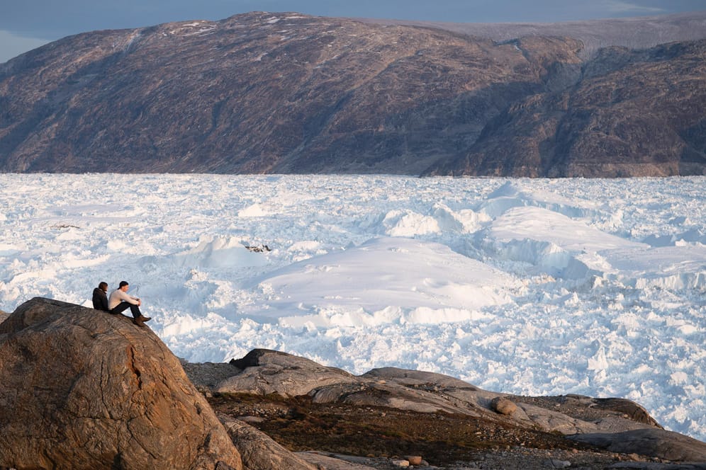 Forscher sitzen auf einem Hügel und blicken auf den Helheim-Gletscher: Von dem riesigen Gletscher in Grönland verschwinden jeden Tag ein paar Meter.