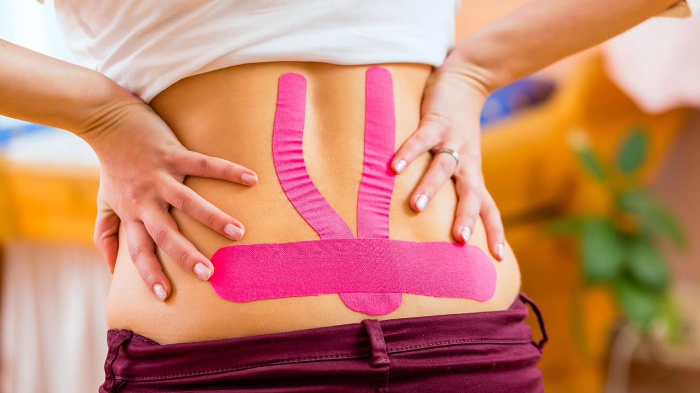 Eine Frau trägt Kinesio-Tape auf dem Rücken: Richtig angebracht helfen die Streifen bei Rückenbeschwerden, Verstauchungen oder Haltungsproblemen.