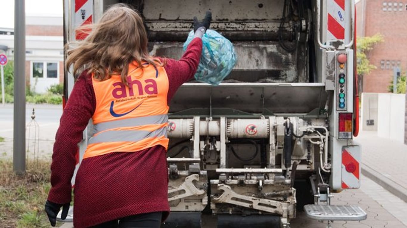 Eine junge Frau wirft bei einem Aktionstag vom Zweckverband Abfallwirtschaft Region Hannover aha einen Sack mit Altpapier in einen Müllwagen.
