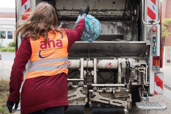 Eine junge Frau wirft bei einem Aktionstag vom Zweckverband Abfallwirtschaft Region Hannover aha einen Sack mit Altpapier in einen Müllwagen.