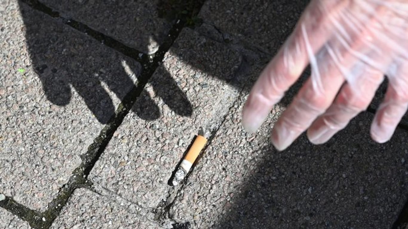Ein Mann sammelt eine Zigarettenstummel vom Boden auf.