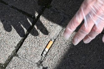 Ein Mann sammelt eine Zigarettenstummel vom Boden auf.