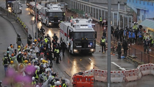 Polizisten stehen neben einem Wasserwerfer.