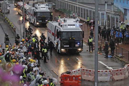 Polizisten stehen neben einem Wasserwerfer.