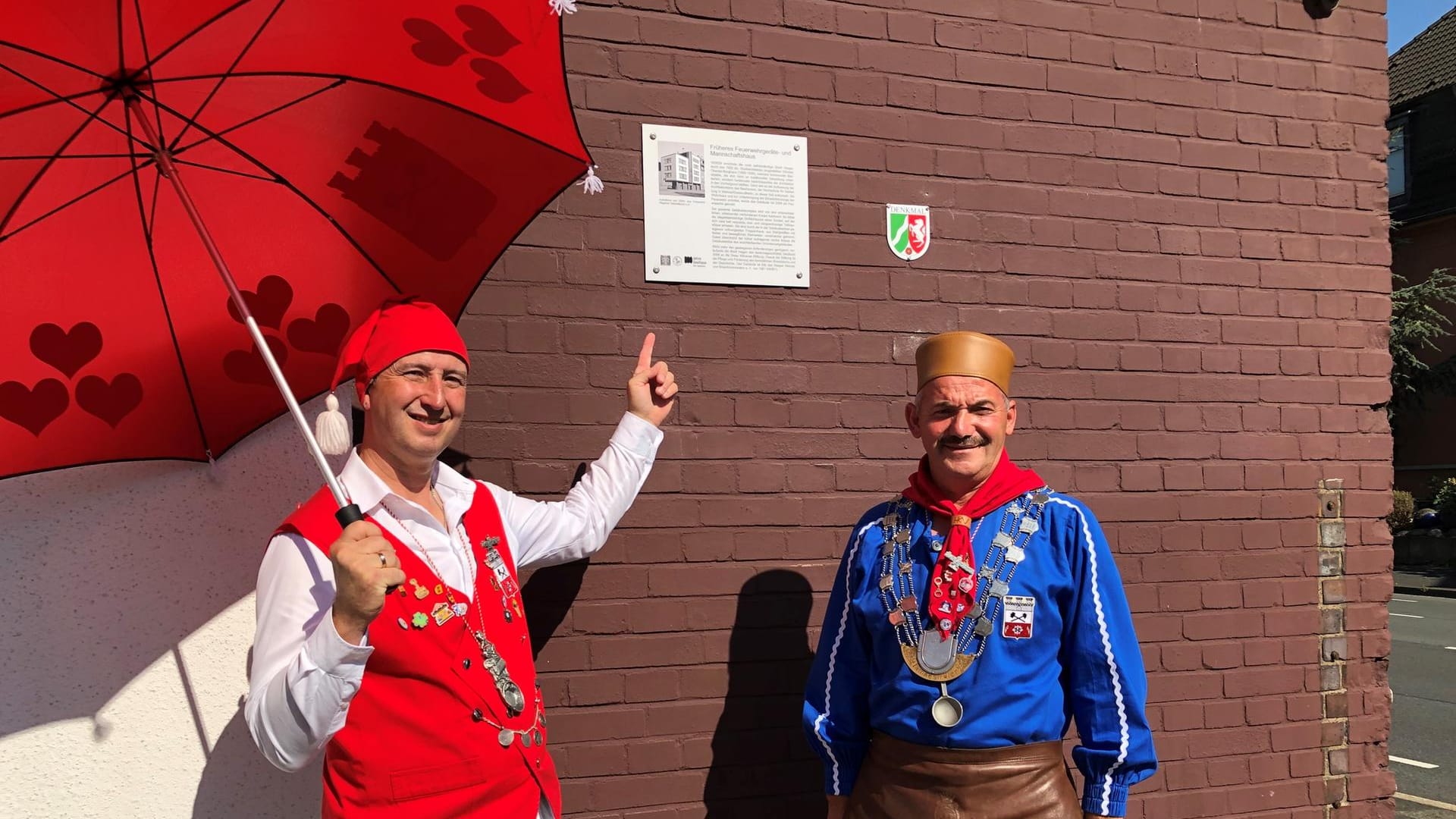 Zwei Männer stehen vor einem Schild: Zwei Symbolfiguren des Hasper Brauchtums, Kirmesbauer Michael Kröner und "Iämpestörter" Thomas Wolter, freuen sich über die neue Tafel an der alten Feuerwache.