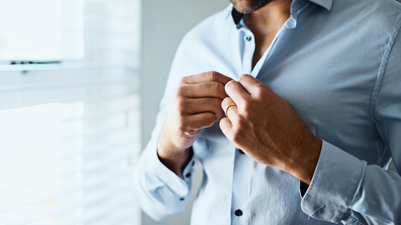 Ein Mann knöpft sein Hemd zu: Stiftung Warentest prüfte 14 hellblaue Business-Hemden aus 100 Prozent Baumwolle.