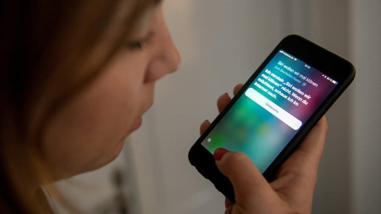 Eine junge Frau bedient auf einem iPhone die Spracherkennung des Apple-Programms Siri.