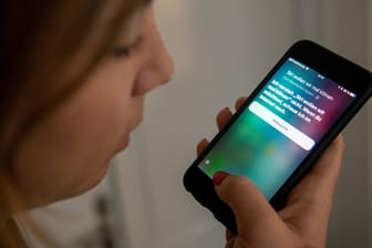 Eine junge Frau bedient auf einem iPhone die Spracherkennung des Apple-Programms Siri.